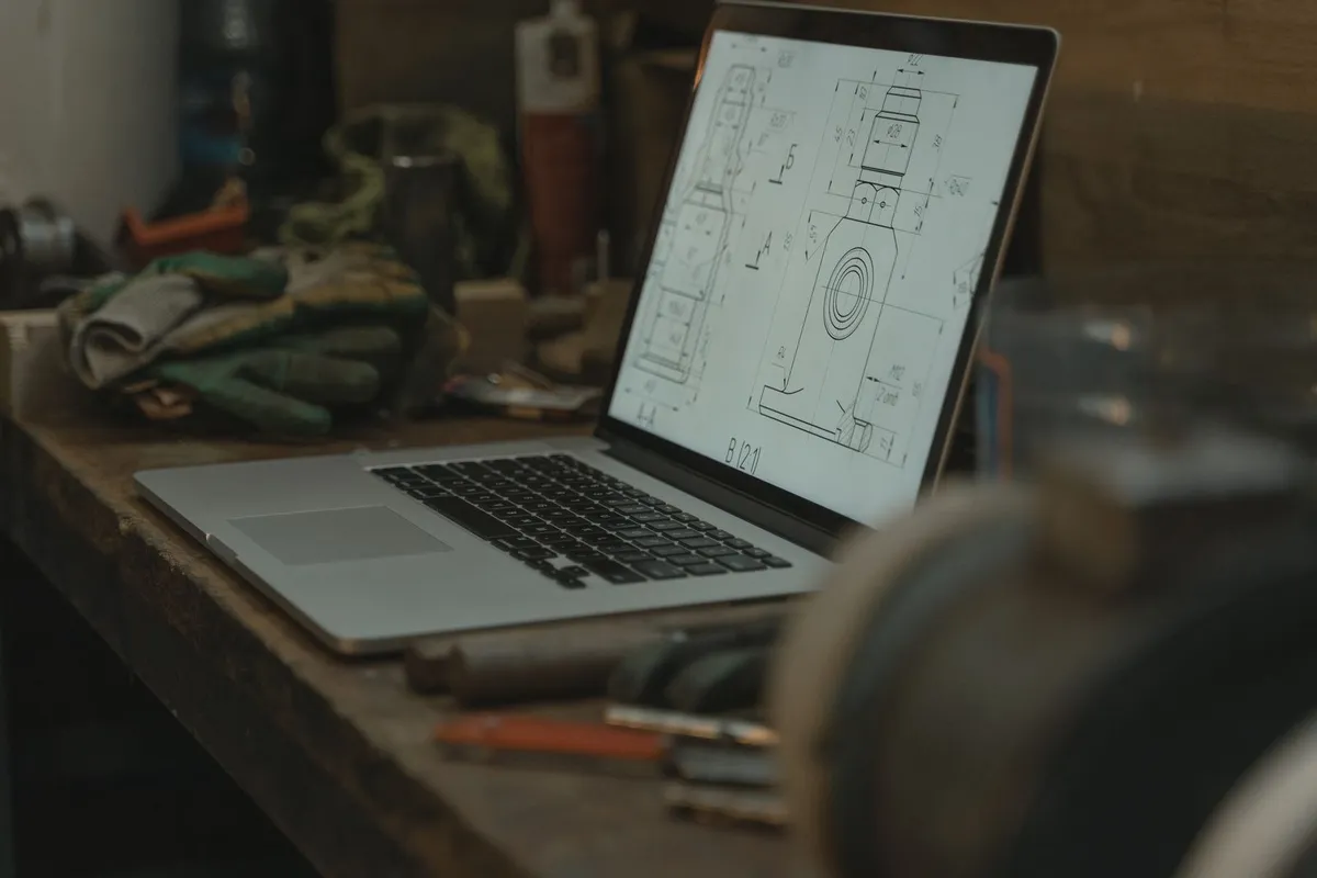 A laptop showing a technical drawing on a workshop bench
